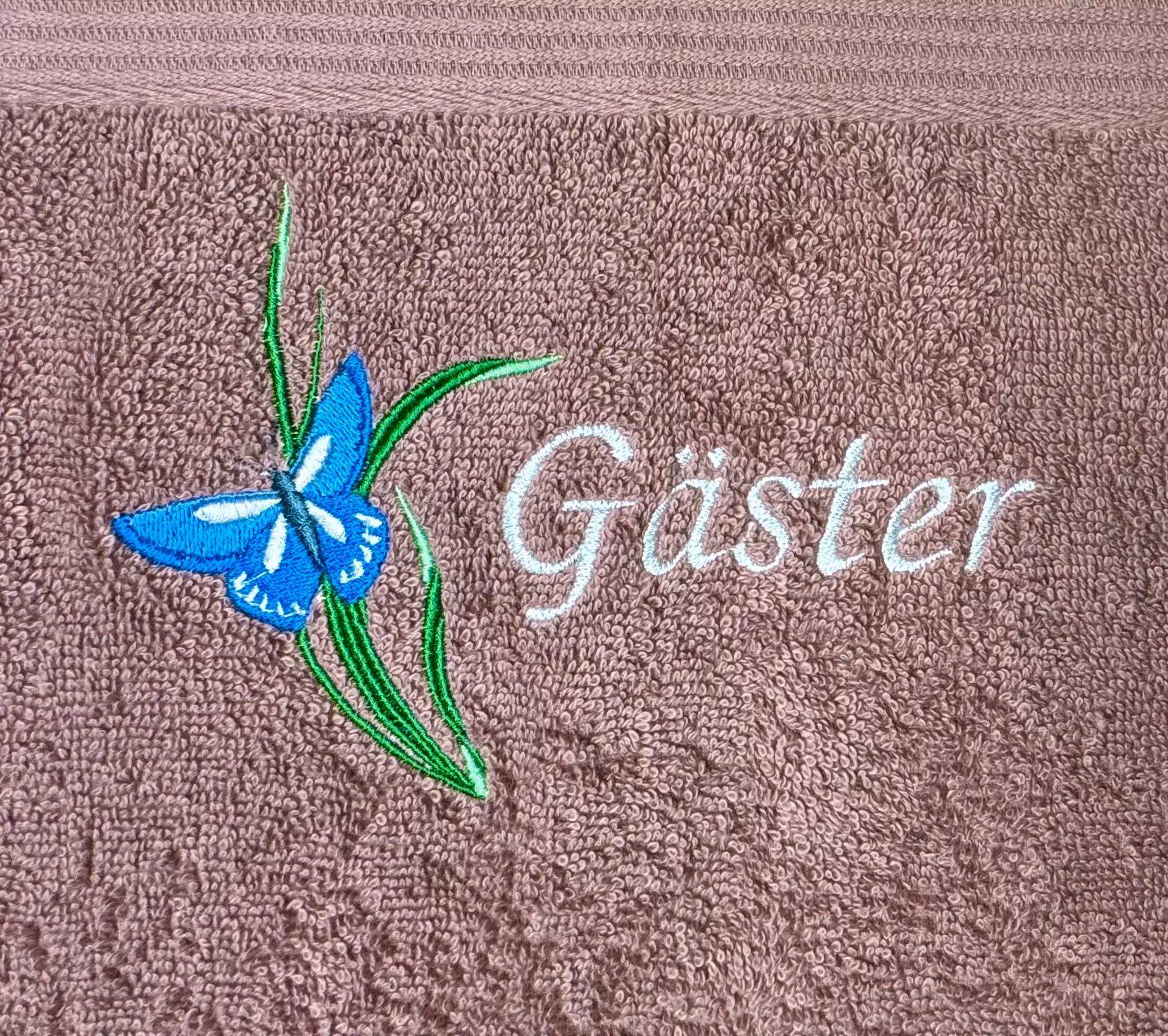 Gammelrosa ästhandduk med en blå  broderad fjäril på ett strå