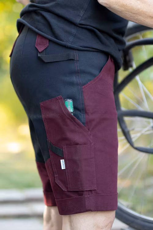 Kvinna som bär vinröda arbetsshorts med stretch när hon lagar sin cykel.