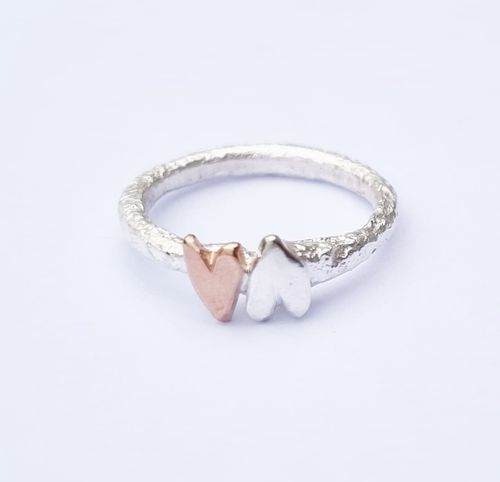 A sparkling and raw silver ring with a bronze heart and a silver heart wrapped around it