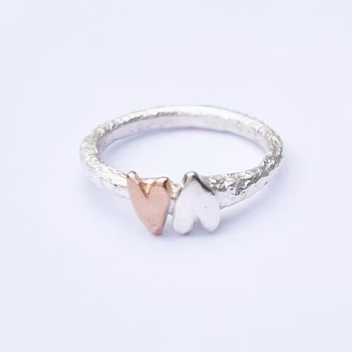 A sparkling and raw silver ring with a bronze heart and a silver heart wrapped around it