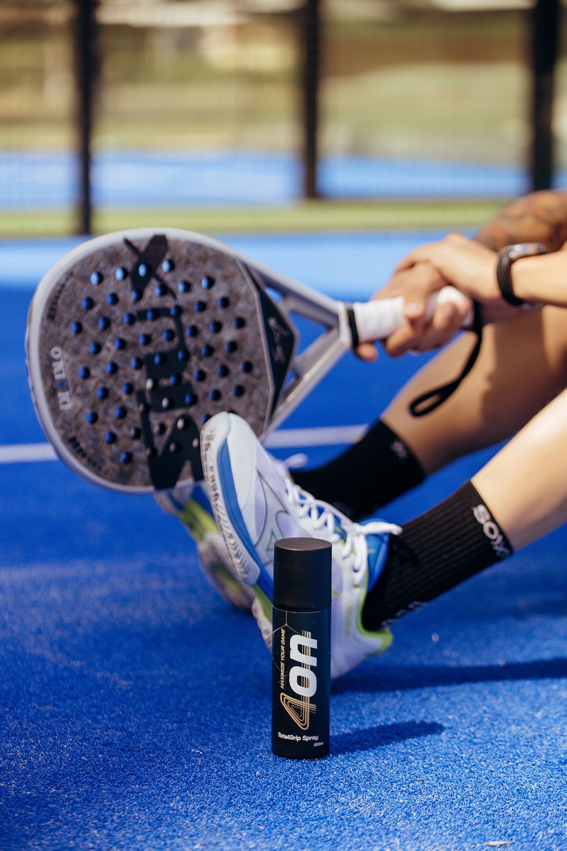 Pro padel player Daniel Sanyo Gutierrez sitting on the court with a 4on TotalGrip spray, holding his racket.