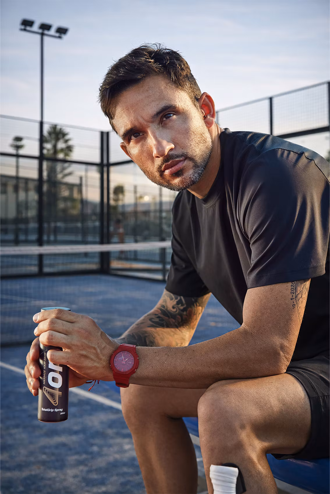 Pro padel player Daniel Sanyo Gutierrez sitting next to the padel court, holding 4on TotalGrip Spray.