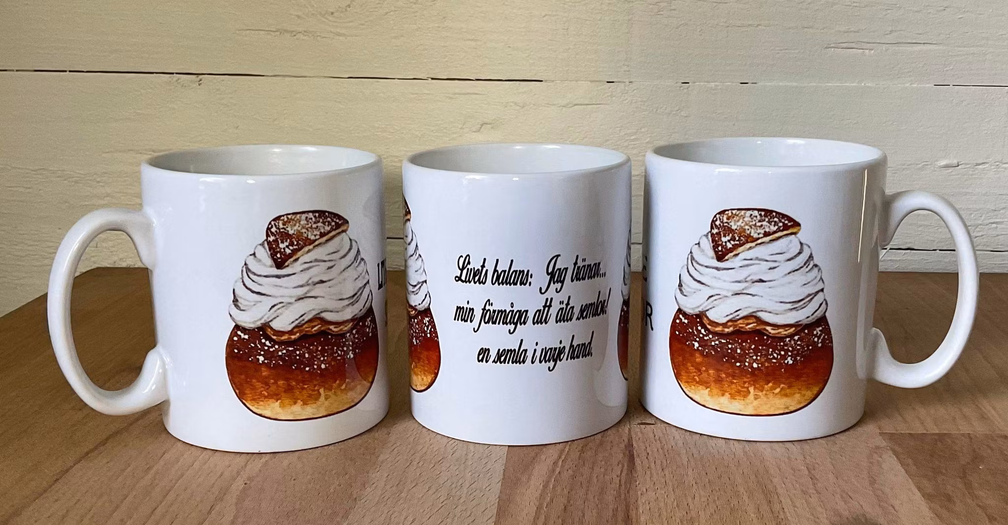 Vit mugg med en bild av en semla och texten Livets balans: en semla i varje hand tryckt på båda sidor, keramik, 330 ml.
