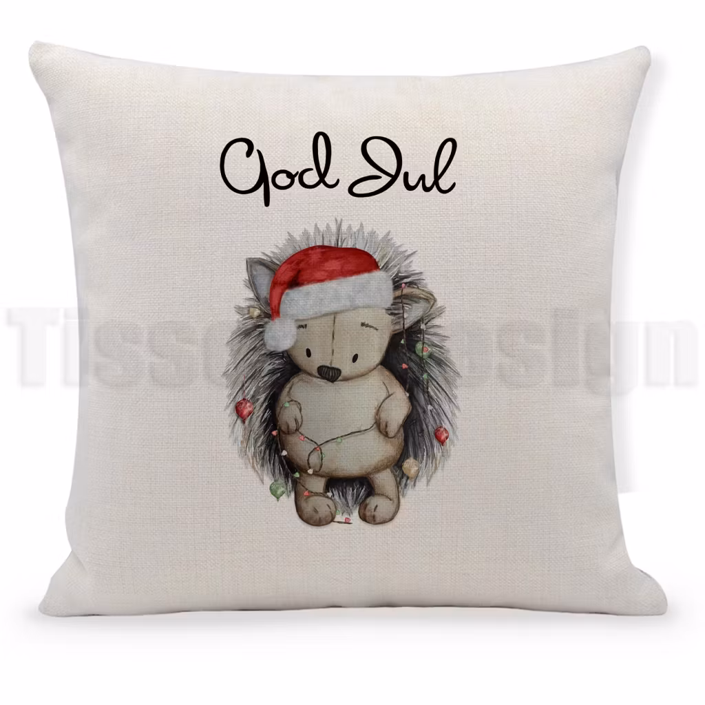 Beige kuddfodral med igelkott i tomteluva och juldekorationer samt texten God Jul.