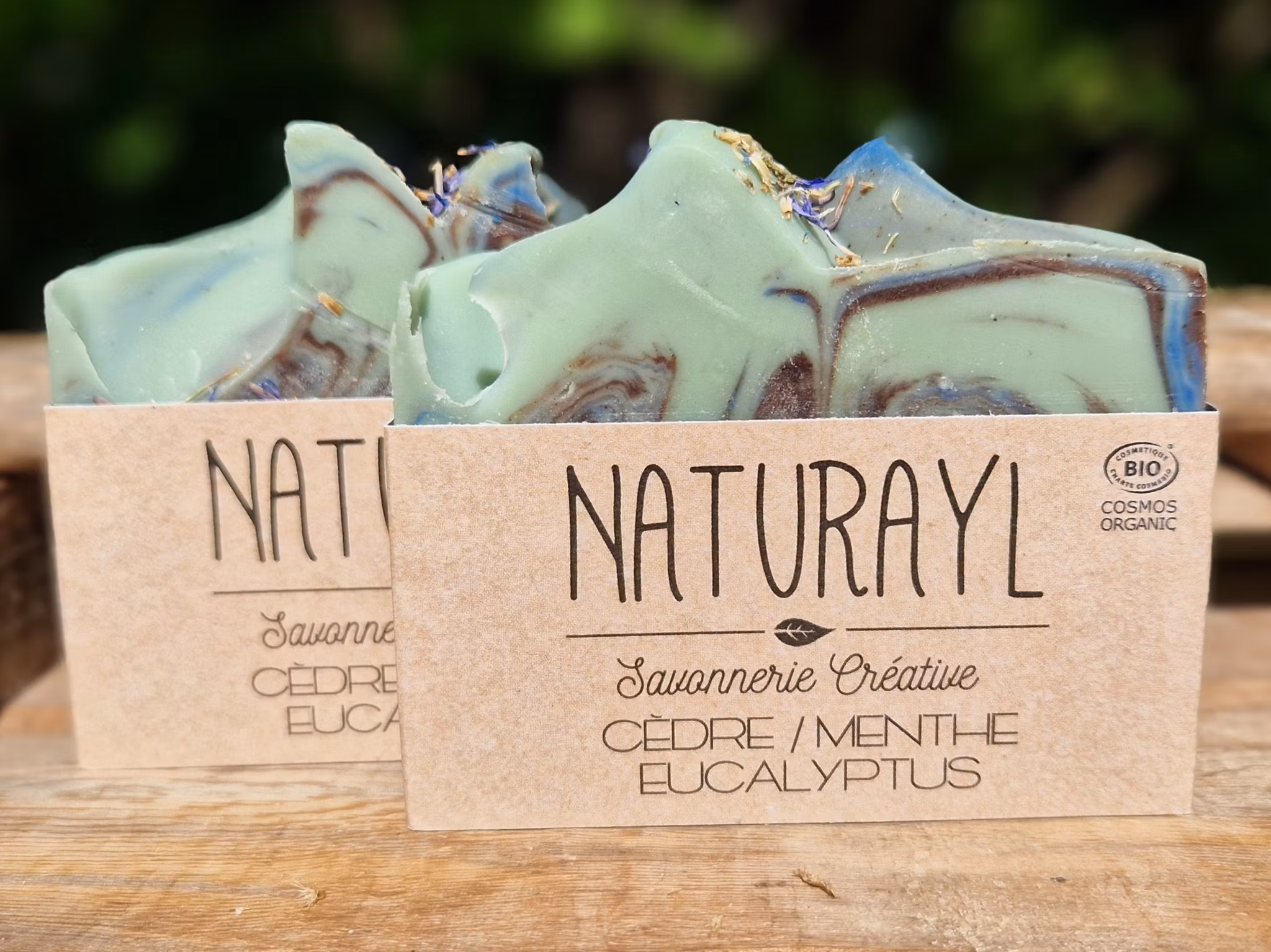 Två skurna tvålar melerade med svirvelmönster i turkos, ljust grön och svart med etikett