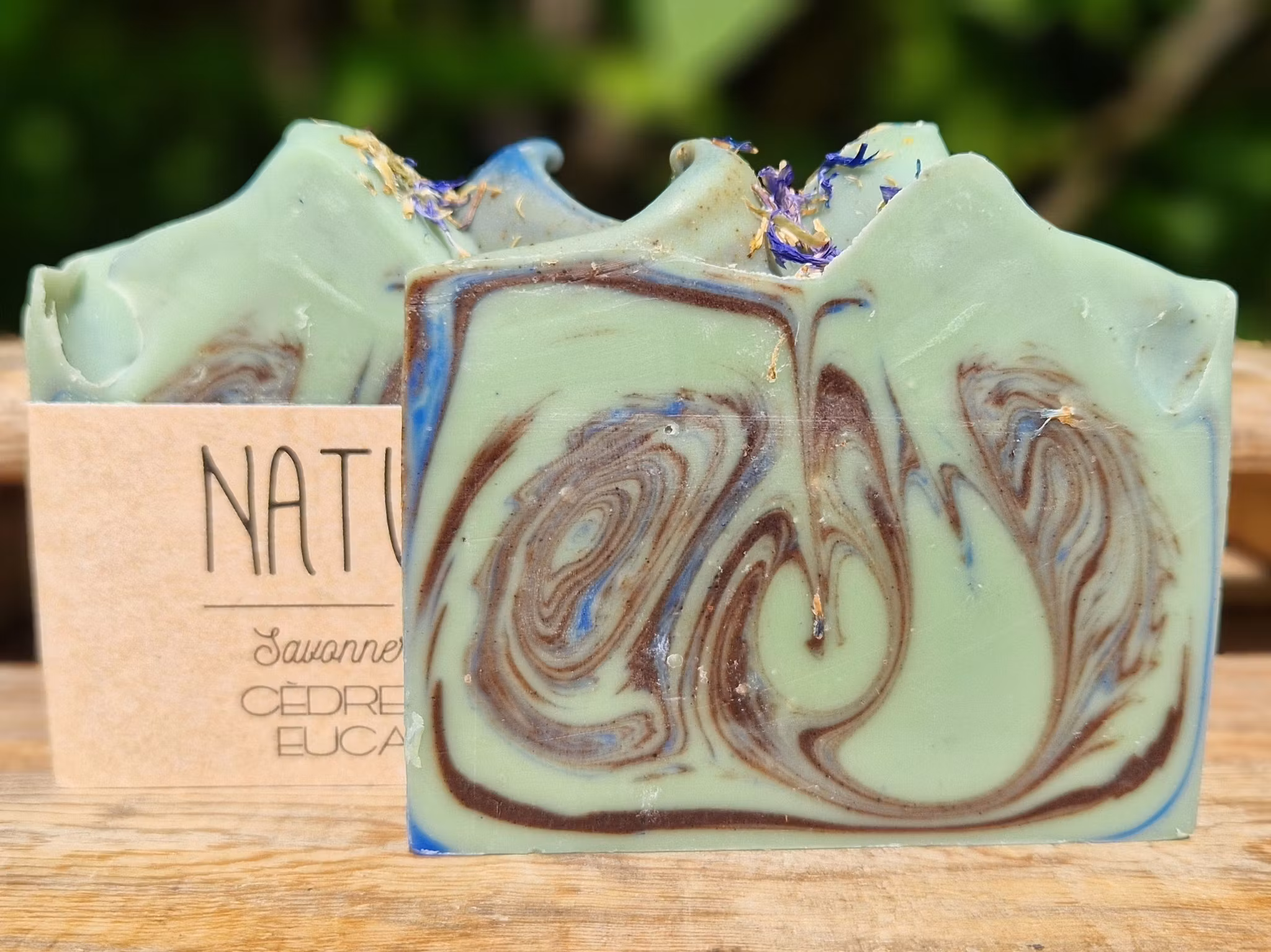 Två skurna tvålar melerade med svirvelmönster i turkos, ljust grön och svart, en utan etikett