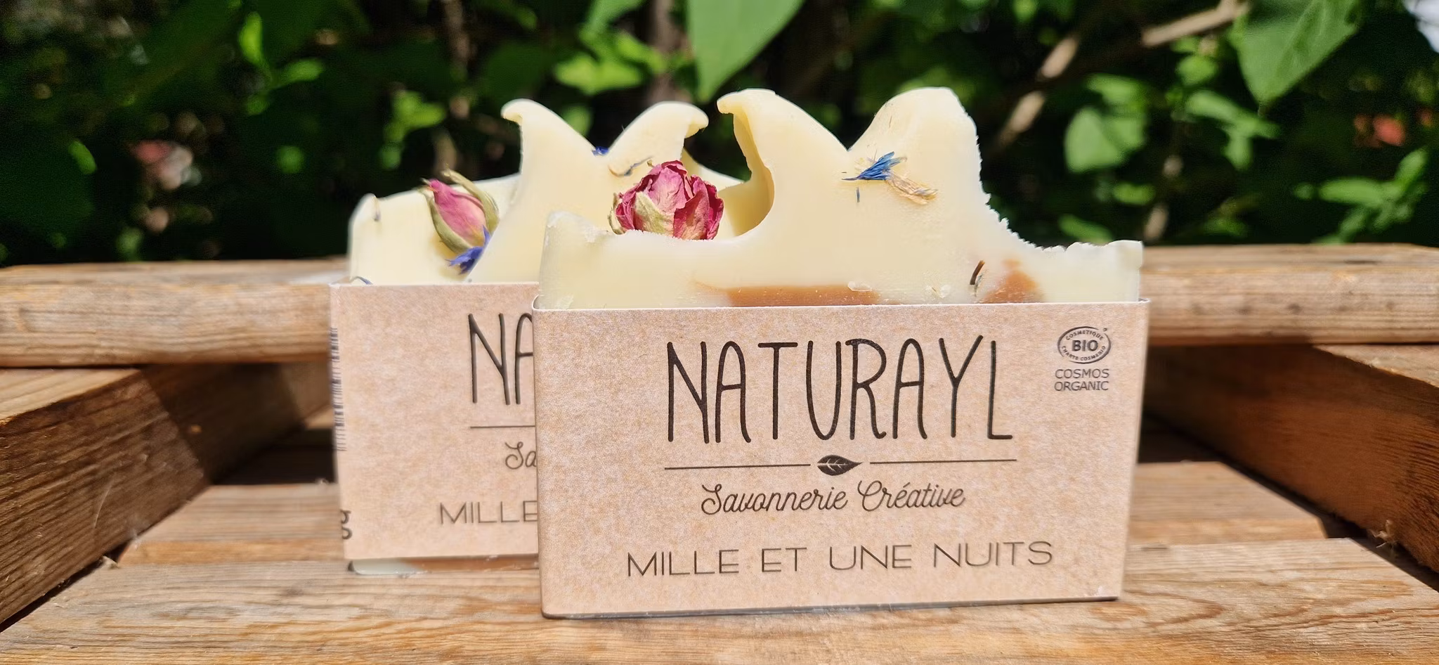 Två krämvita skurna tvålar med rosknopp på toppen, med brun och brunrött område i mitten av tvålen och etikett