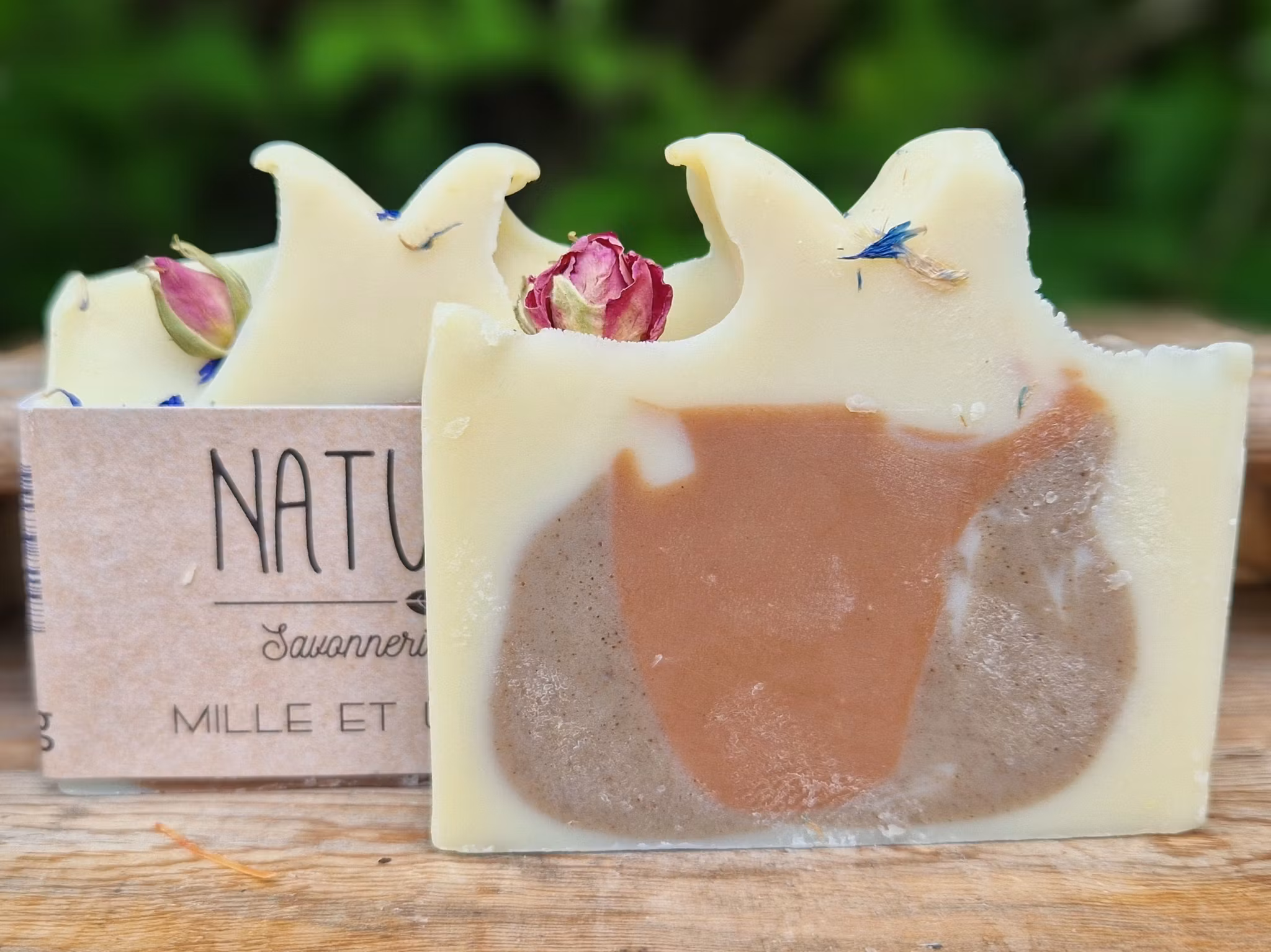 Två krämvita skurna tvålar med rosknopp på toppen, med brun och brunrött område i mitten av tvålen, en utan etikett.