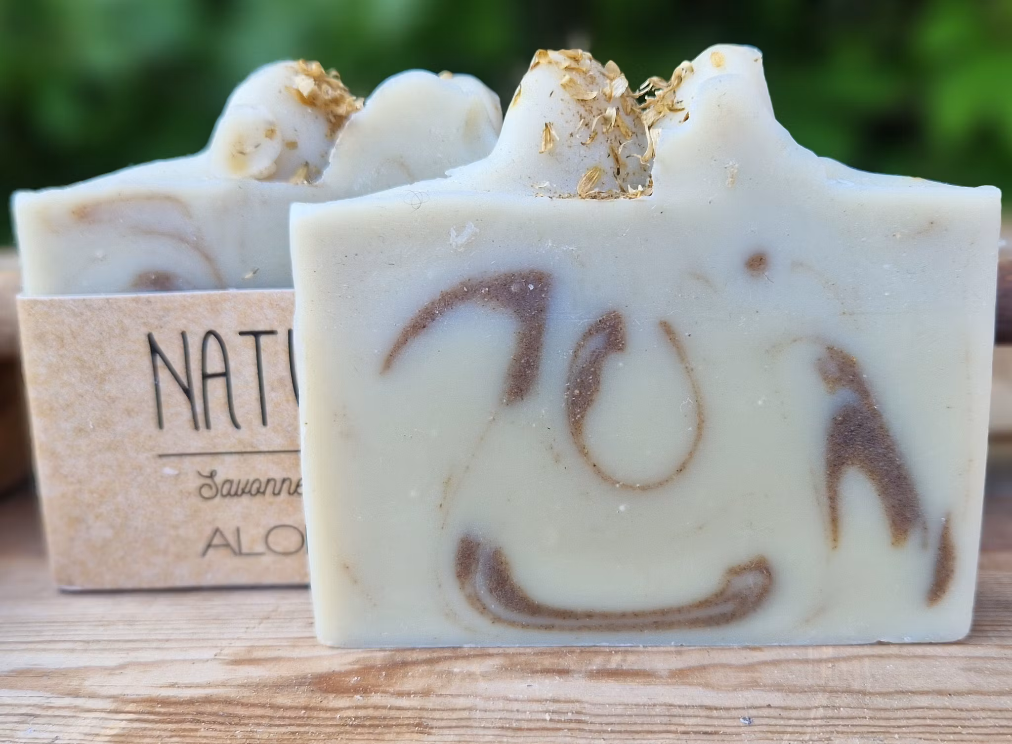 Två beigevita skurna tvålar med brun marmoring i tvålens mitt, en tvål med etikett och en utan etikett