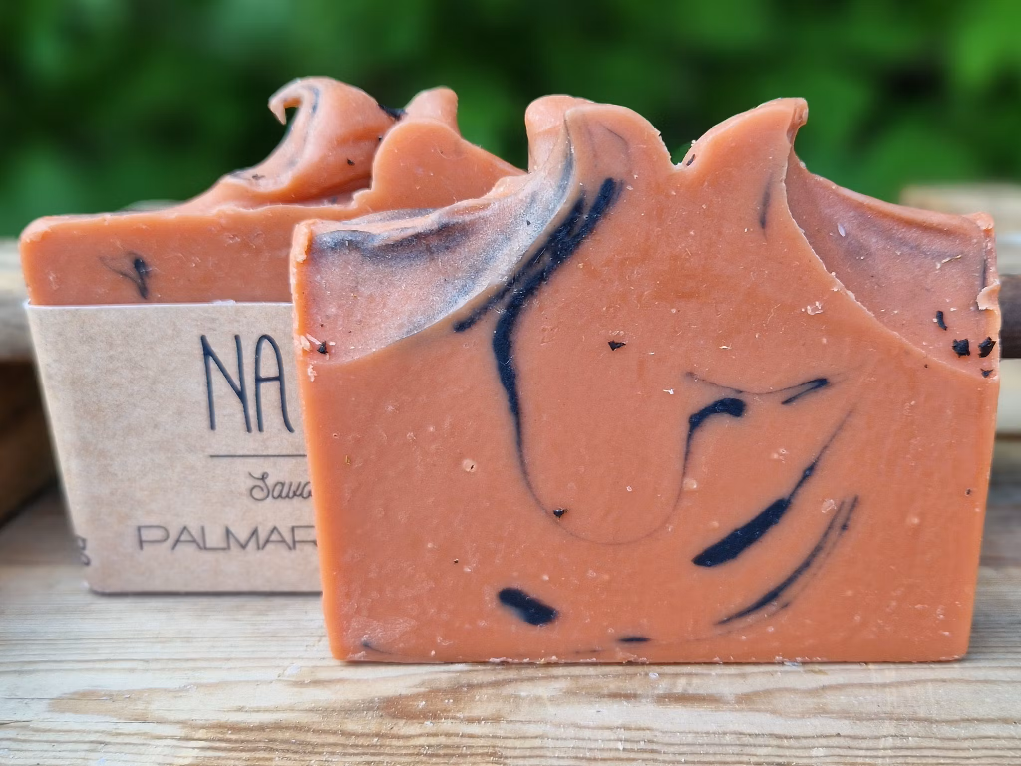 Två skurna rödbruna tvålar med svart marmorering, en tvål med etikett och en utan etikett.