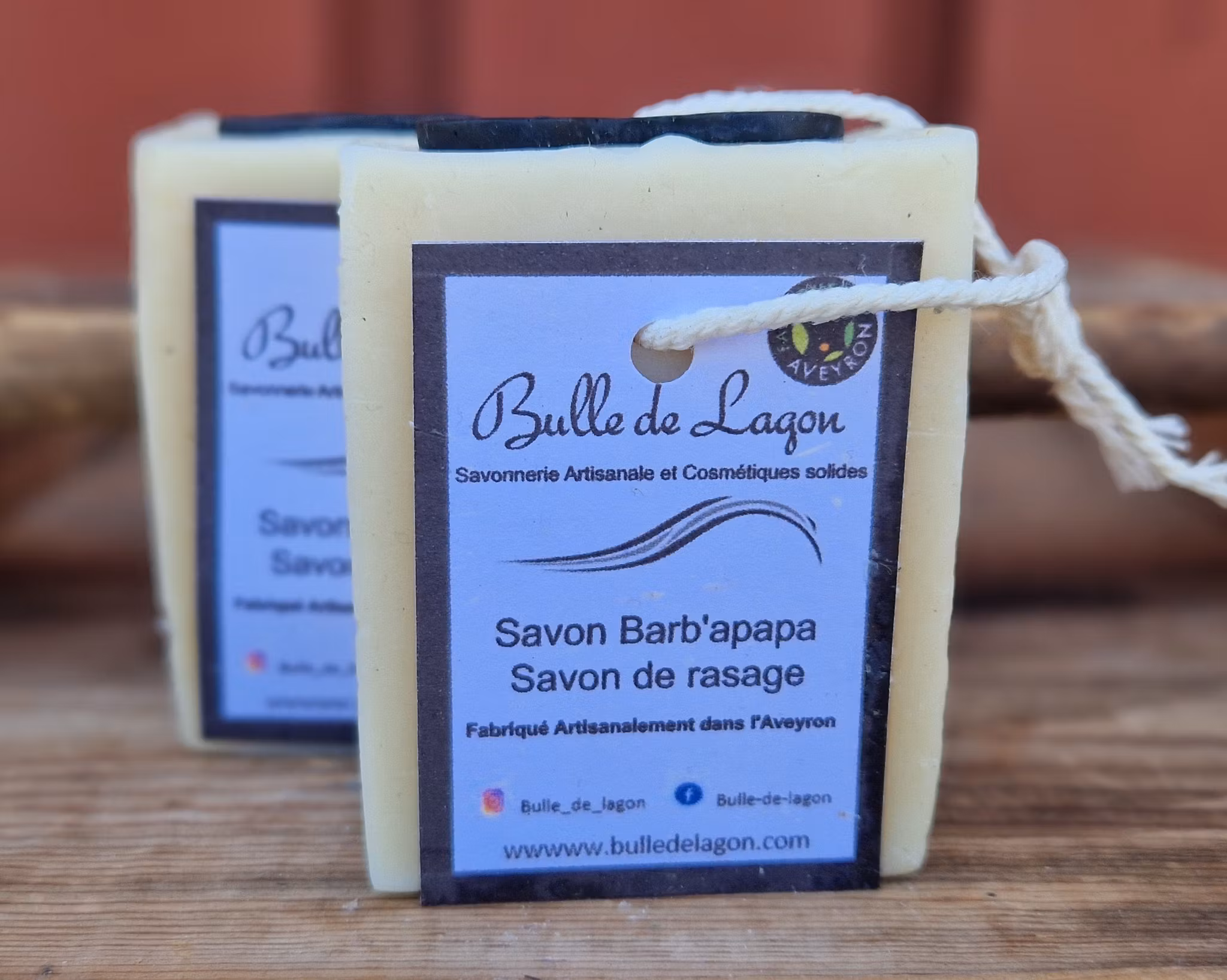 Två krämfärgade rektangulära tvålar med svart mustach ovanpå, etikett och snöre för upphängning