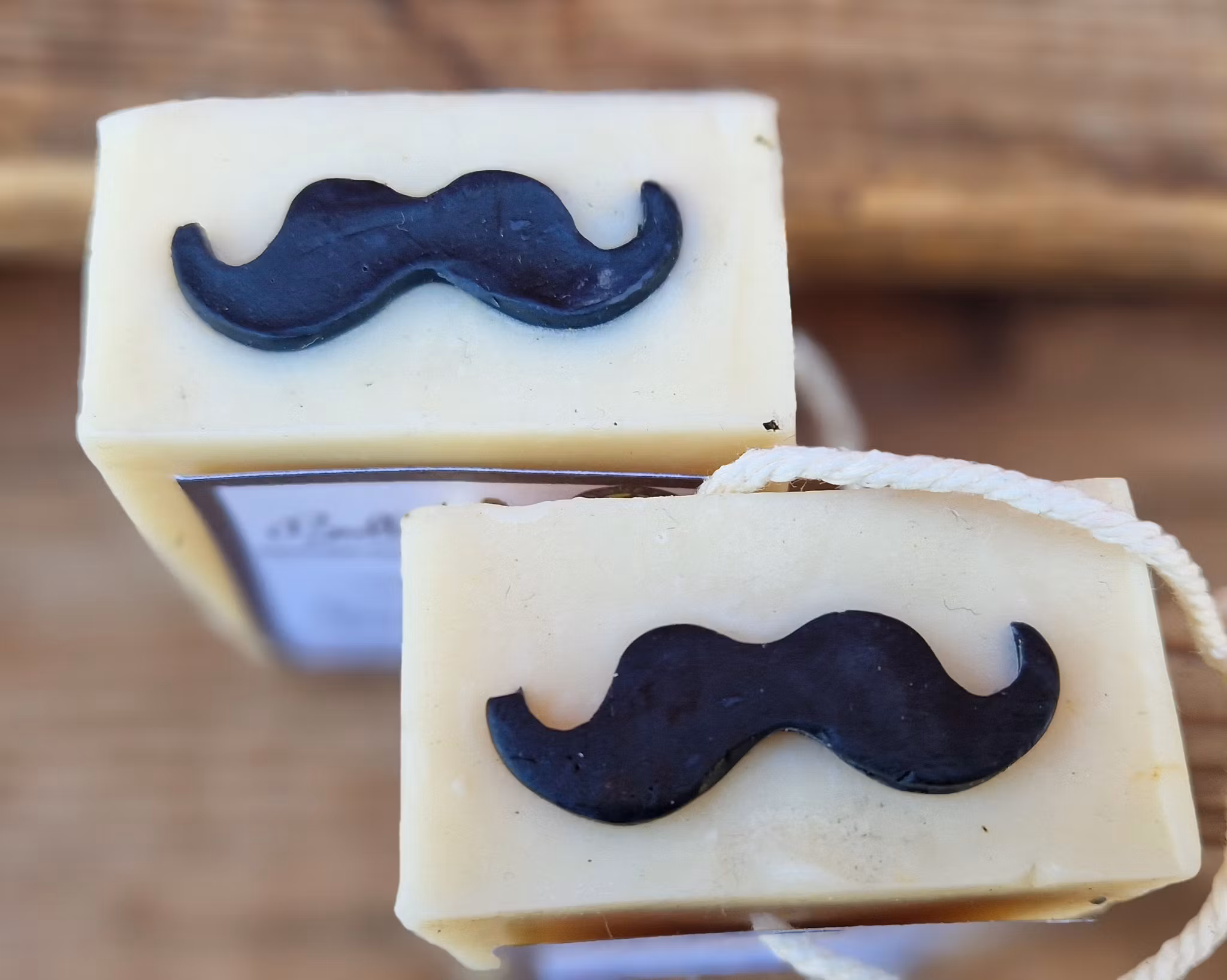 Närbild på ovansidan av två krämvita tvålar med en svart mustach på varje tvål