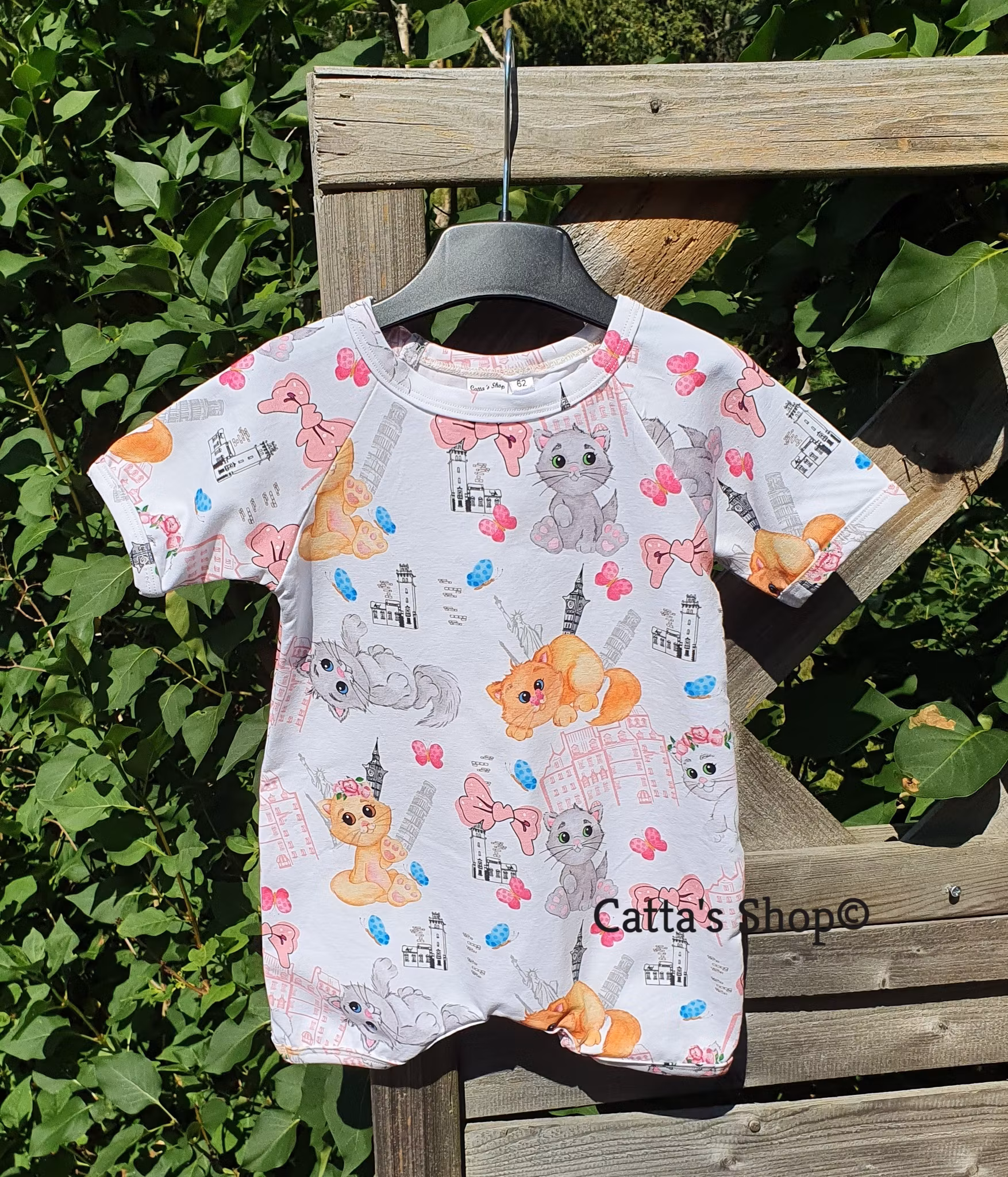 Bilden föreställer en jumpsuit med korta ärmar och ben, motiv lekande katter i ekologisk jersey/trikå