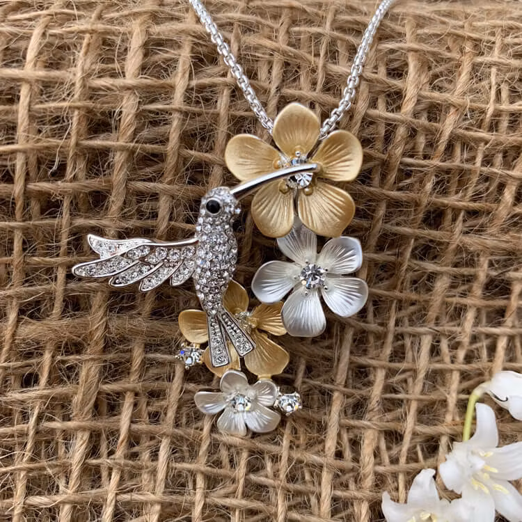 Halsband med blommor i guld och silvertoner samt en gnistrande kolibri.