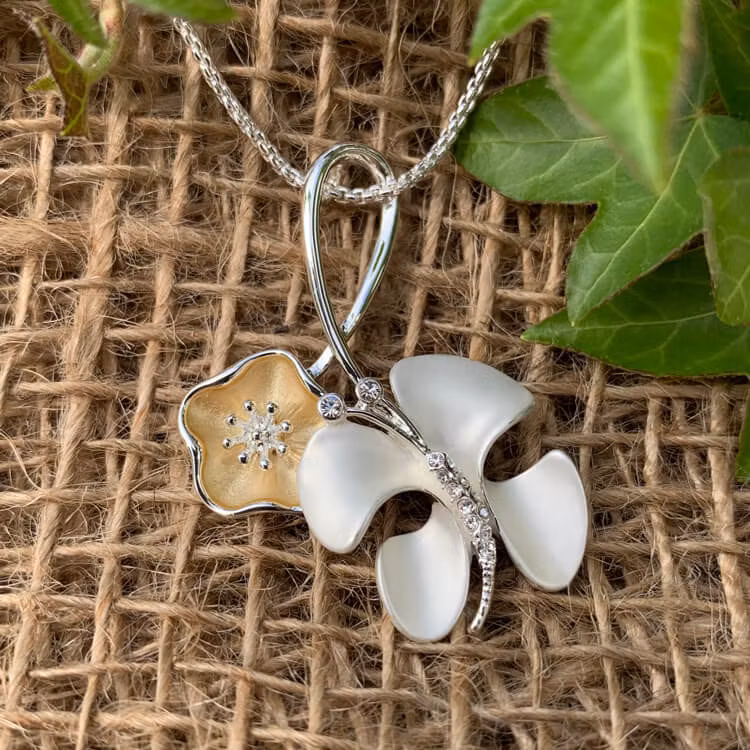 Halsband med en abstrakt fjäril samt en blomma i silver- och guldtoner.