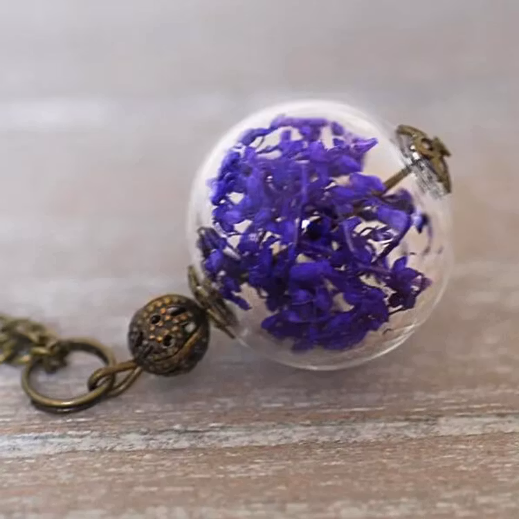 Bild på halsband med torkade lila blommor i glaskula med bronskedja.