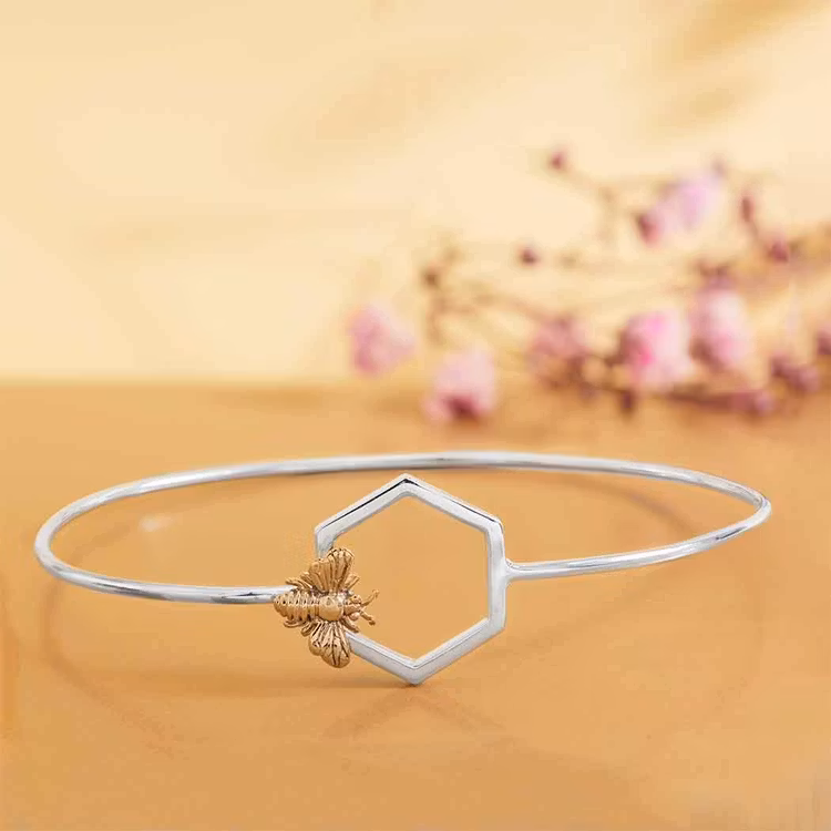 Silverarmband med ett bronsbi i ena änden som krokas fast i en silverhexagon i andra änden.