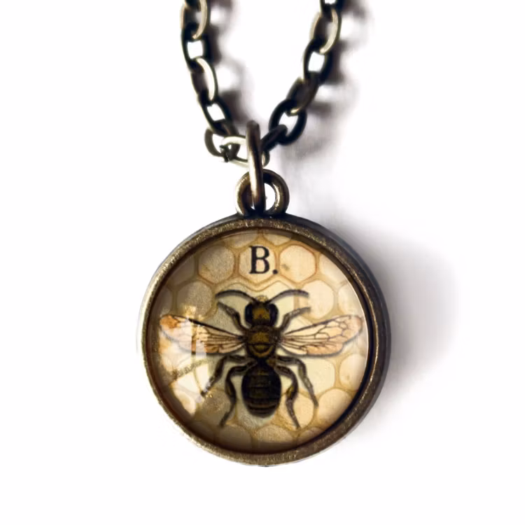 Bild på ett vintageinspirerat halsband i mässing med illustrationer av ett bi.