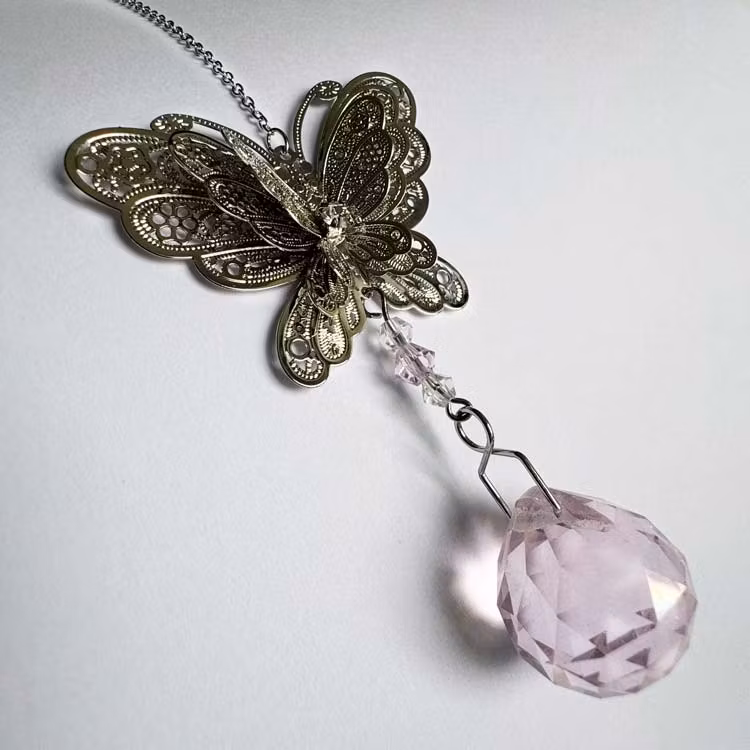 Solfångare med silverfärgad fjäril och rosa prisma.