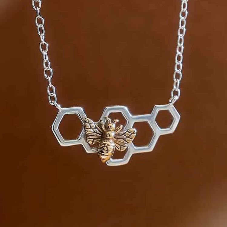Bild som visar ett silverhalsband som föreställer en liten bit vaxkaka med ett bronsbi på.