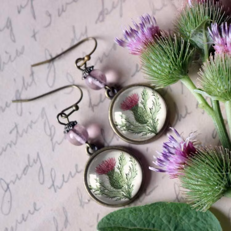 Örhängen med pärlor och illustrationer av tistlar under cabochoner av glas.