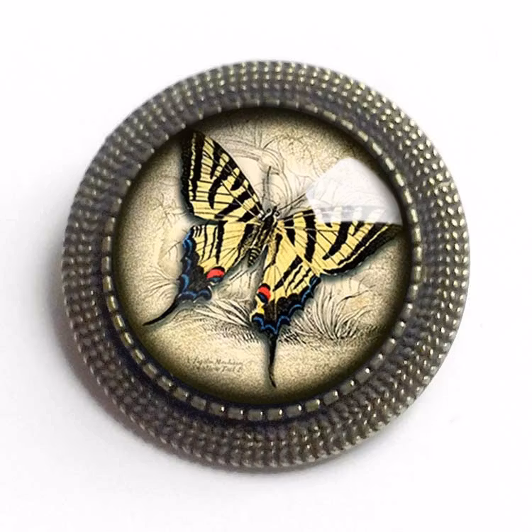 Vintageinspirerad brosch med en illustration av en gul fjäril under en cabochon av glas.