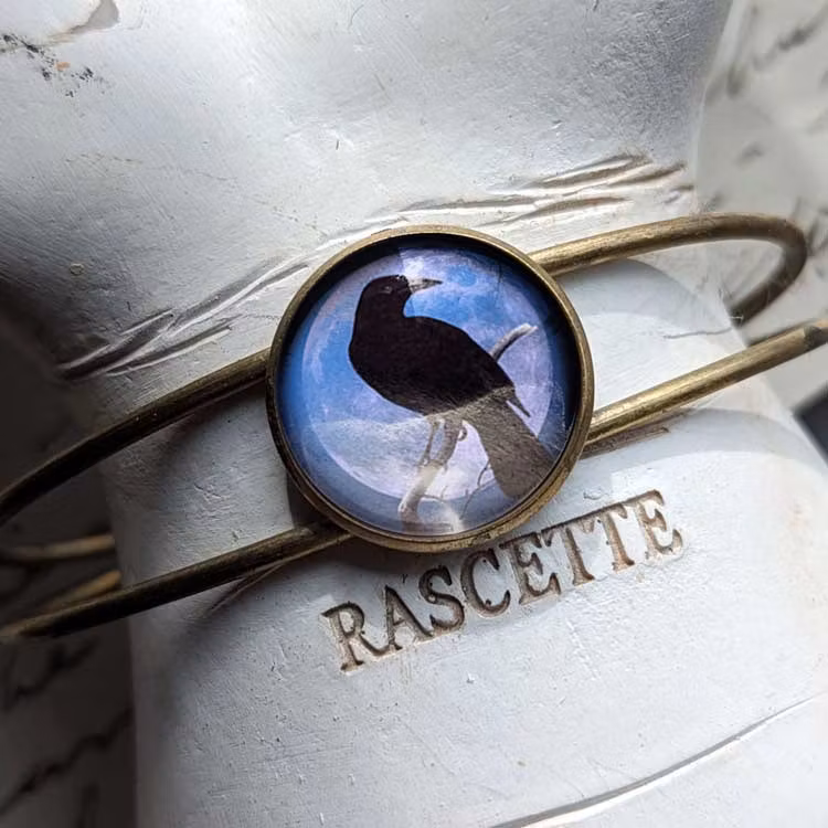 Vintageinspirerat manschettarmband med en illustration av en kråkfågel.