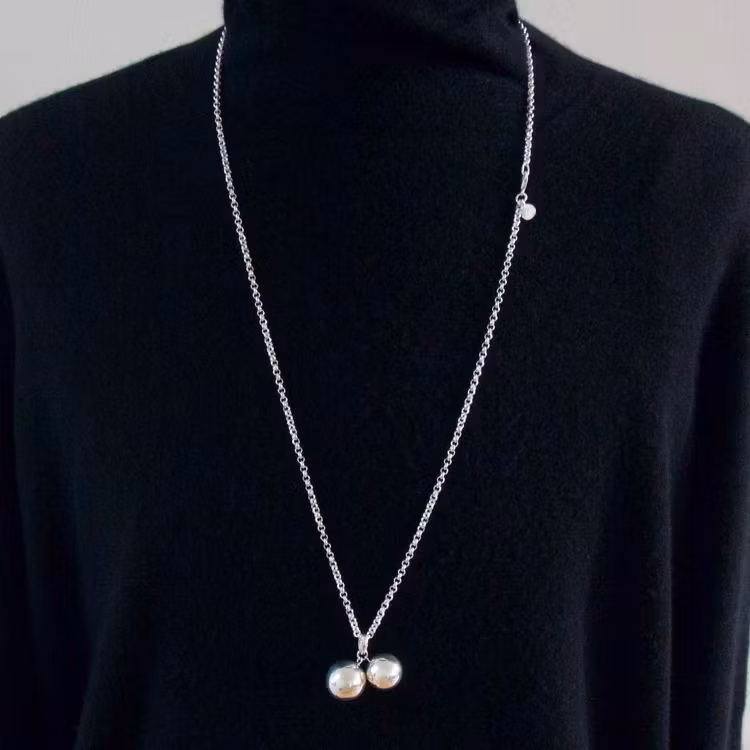 Kvinna med långt halsband med två silverkulor. Woman with long necklace and silver pendant with two silver globes.