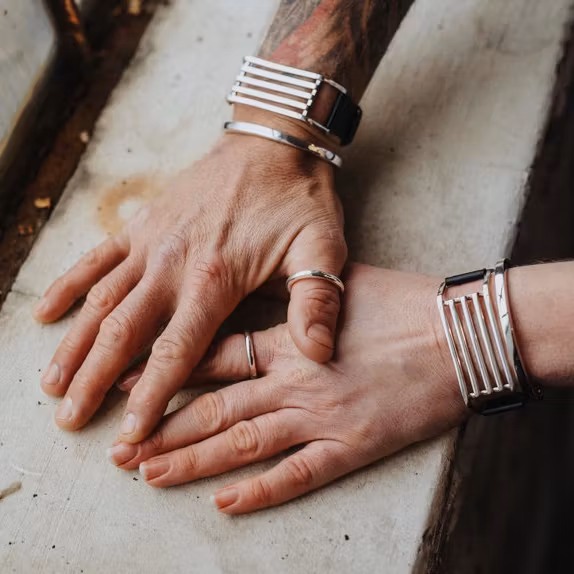 En manshand och en kvinnohand, bägge med samma unisexsmycken, silverring och armband. man and woman wearing the same jewellery, silver ring and bracelets.