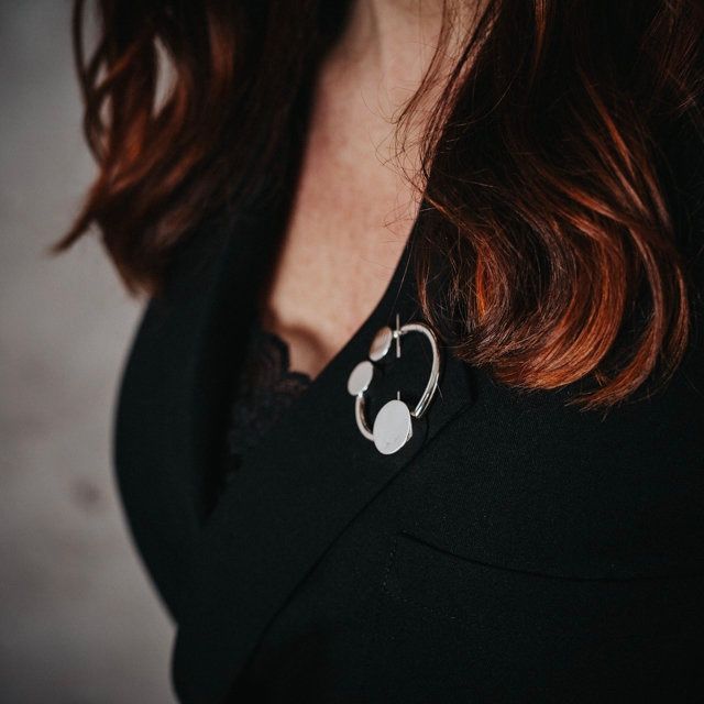 rund silverbrosch med form av omega på kavajslag. round silver brooch with the design from omega on a jacket