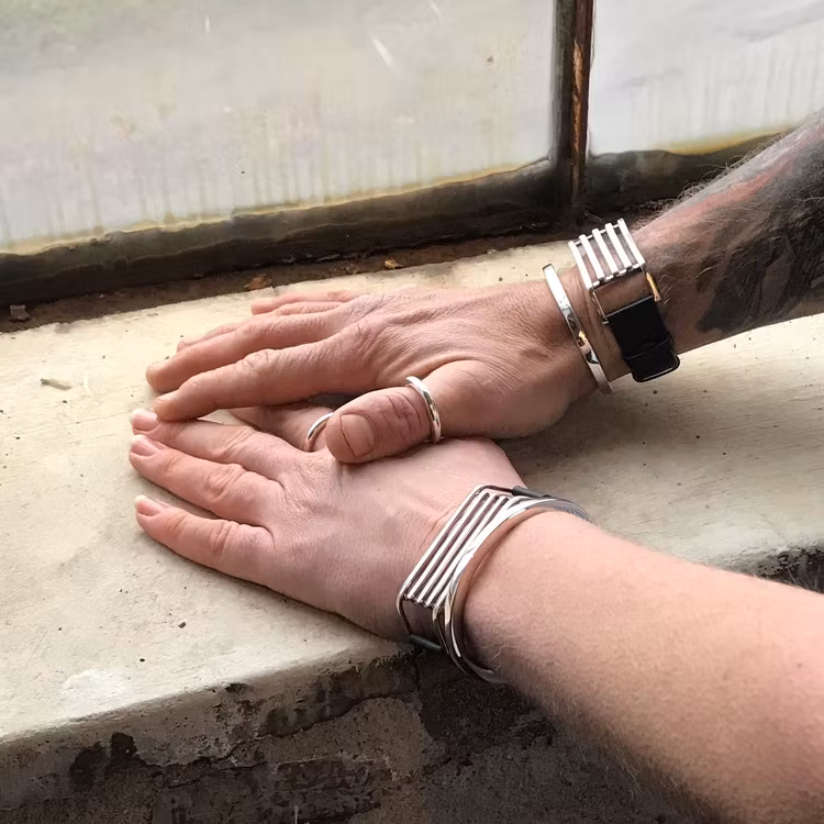 En manshand och en kvinnohand, bägge med samma unisexsmycken, släta silverringar och silverarmband med läder. man and women wearing the same jewelry, bracelets and silver rings, unisex.