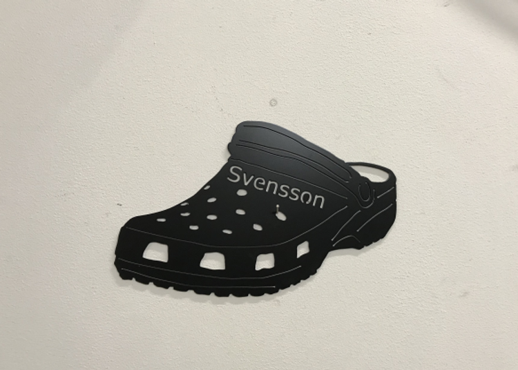 Foppatoffla med texten svensson som är svartlackerad och i plåt.