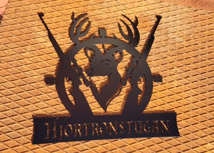 Svart skylt skuren i metall mot rostig bakgrund.