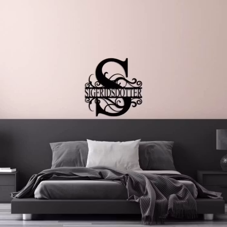 Svart monogram ett stort S och namnet Sigfridsdotter monterat på väggen över en säng.