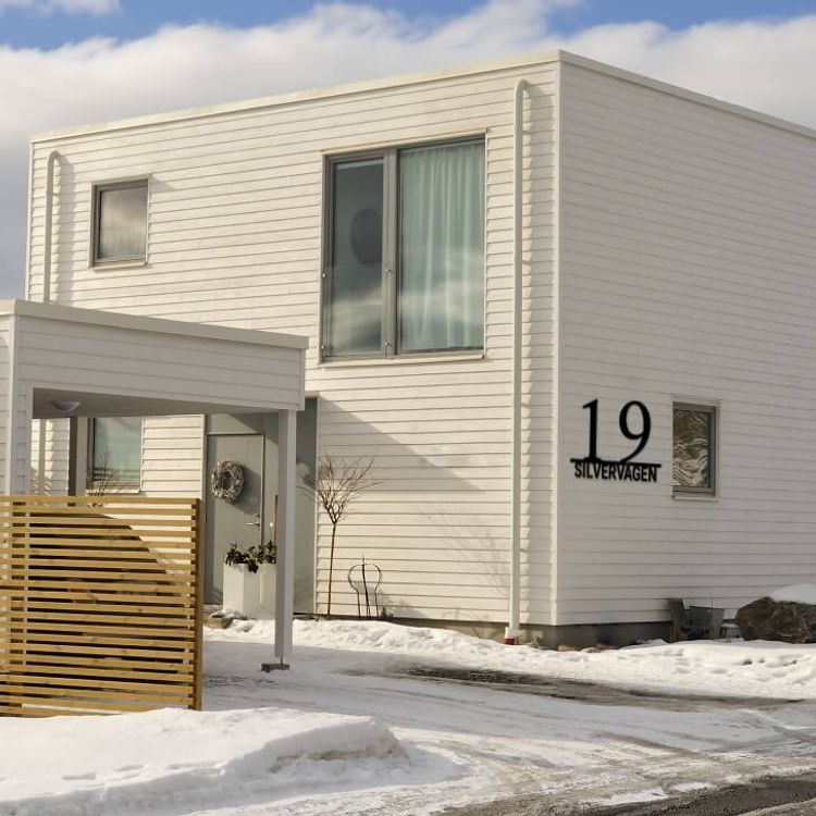 Stilrent husnummer med gatunamn, monterat på vitt modernt hus.