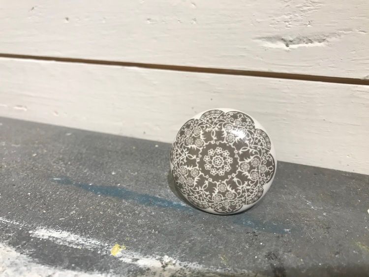 Vit knopp i keramik med grå blomma på framsidan.