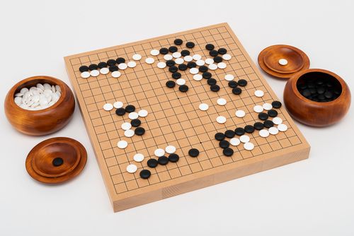 Traditionellt Go-spel med stenar i snäckskal och skiffer, tjockt bräde i bokfanér och träskålar