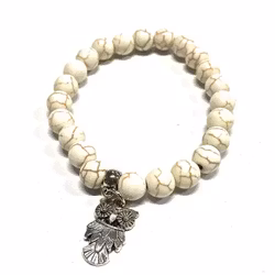 Armband med pärlor och en uggleberlock i polystone med elastiskt band. Art.nr: H 02008. Färg: Off-white.