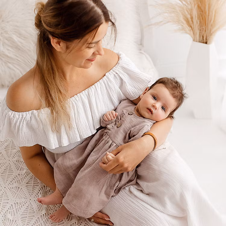 Mamma som håller i bebis i beige muslin klänning