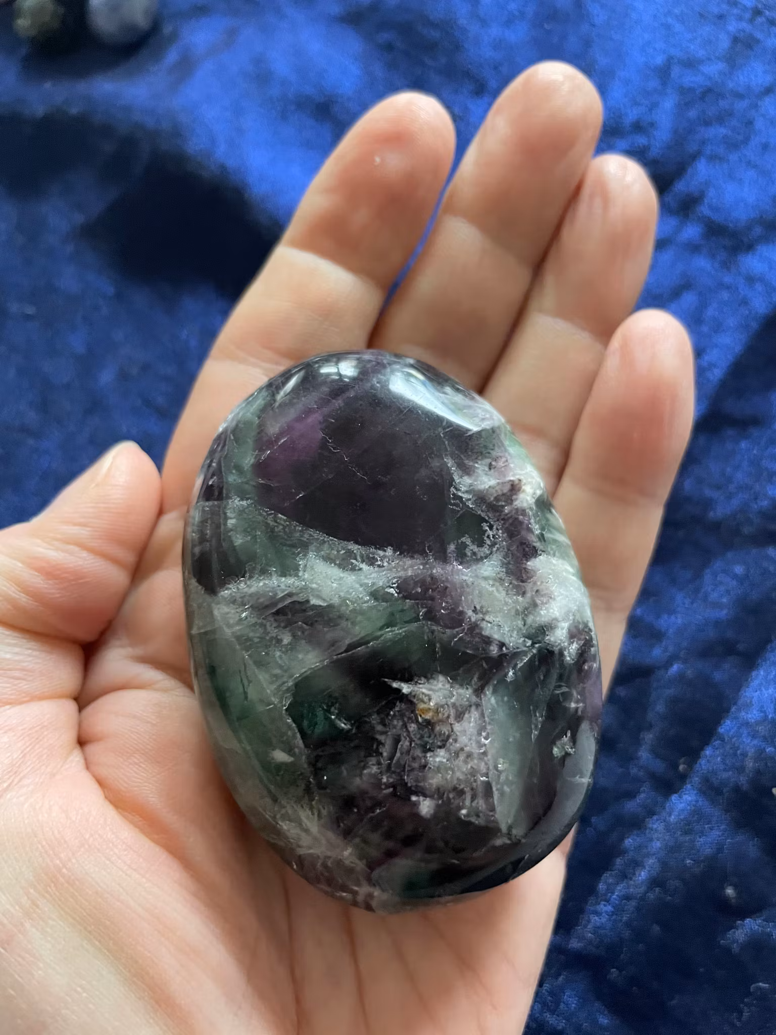 Bilden visar en regnbågsfluorit i palmstone liggande i en hand