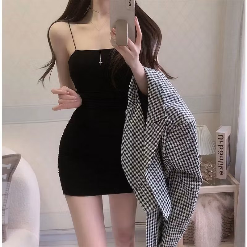 Figure-hugging black mini dress with spaghetti straps paired with a casual plaid jacket for a chic layered look
