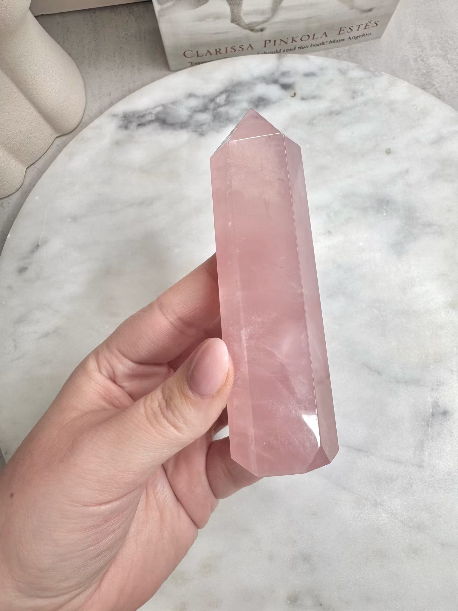 Handhållen polerad spets i ljusrosa rosenkvarts med klar lyster, fotograferad mot vit marmorbakgrund
