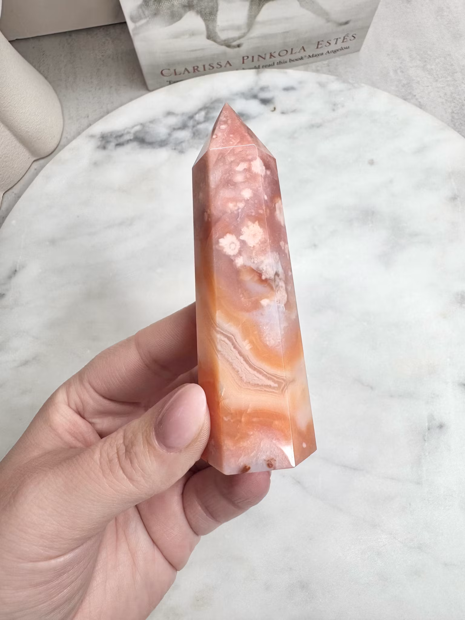 Hand som håller i en kristallspets i rosa och persikotoner med naturliga blomliknande mönster