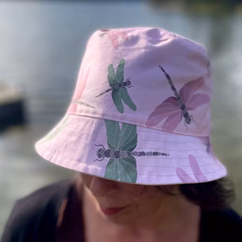 en "sassy n swag"-hatt med det mellanbreda brättet i mönstret Maarit, med sländor på rosa