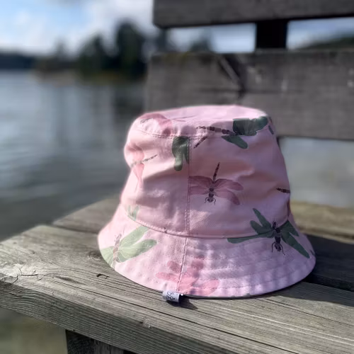 en "sassy n swag"-hatt med det mellanbreda brättet i mönstret Maarit, med sländor på rosa