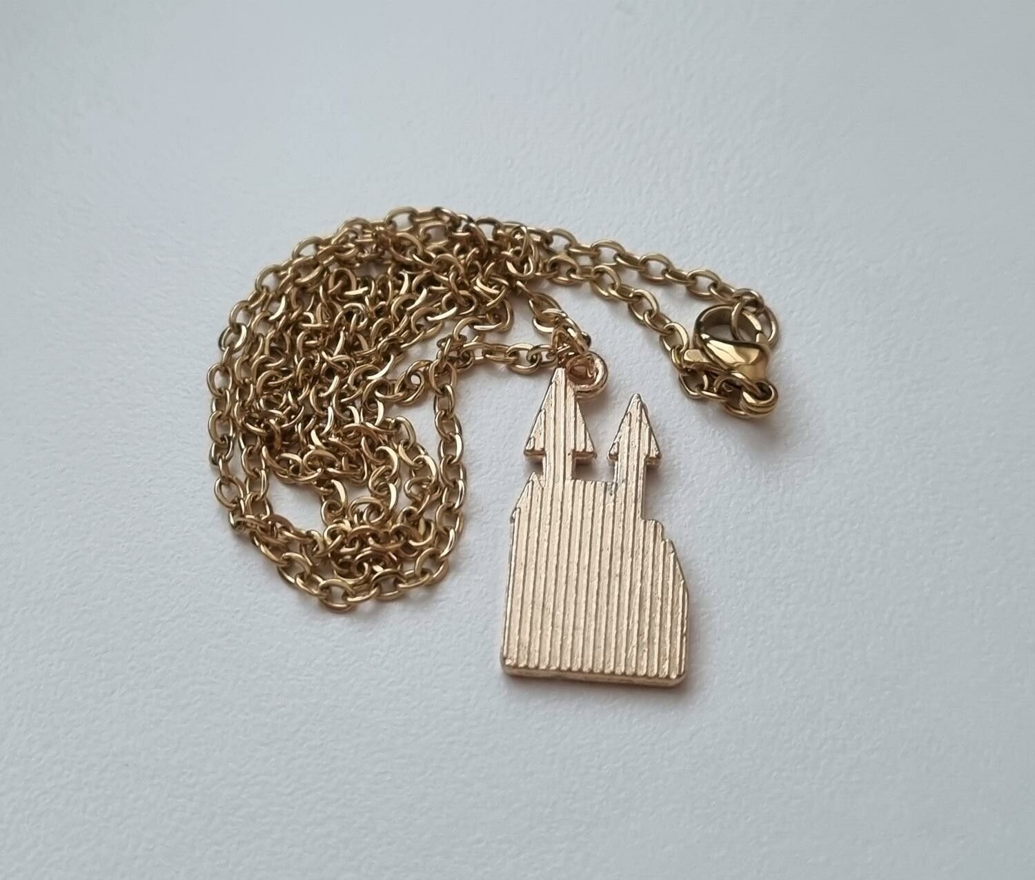 Guldfärgat halsband med ett vitt slott. Berlock / charm