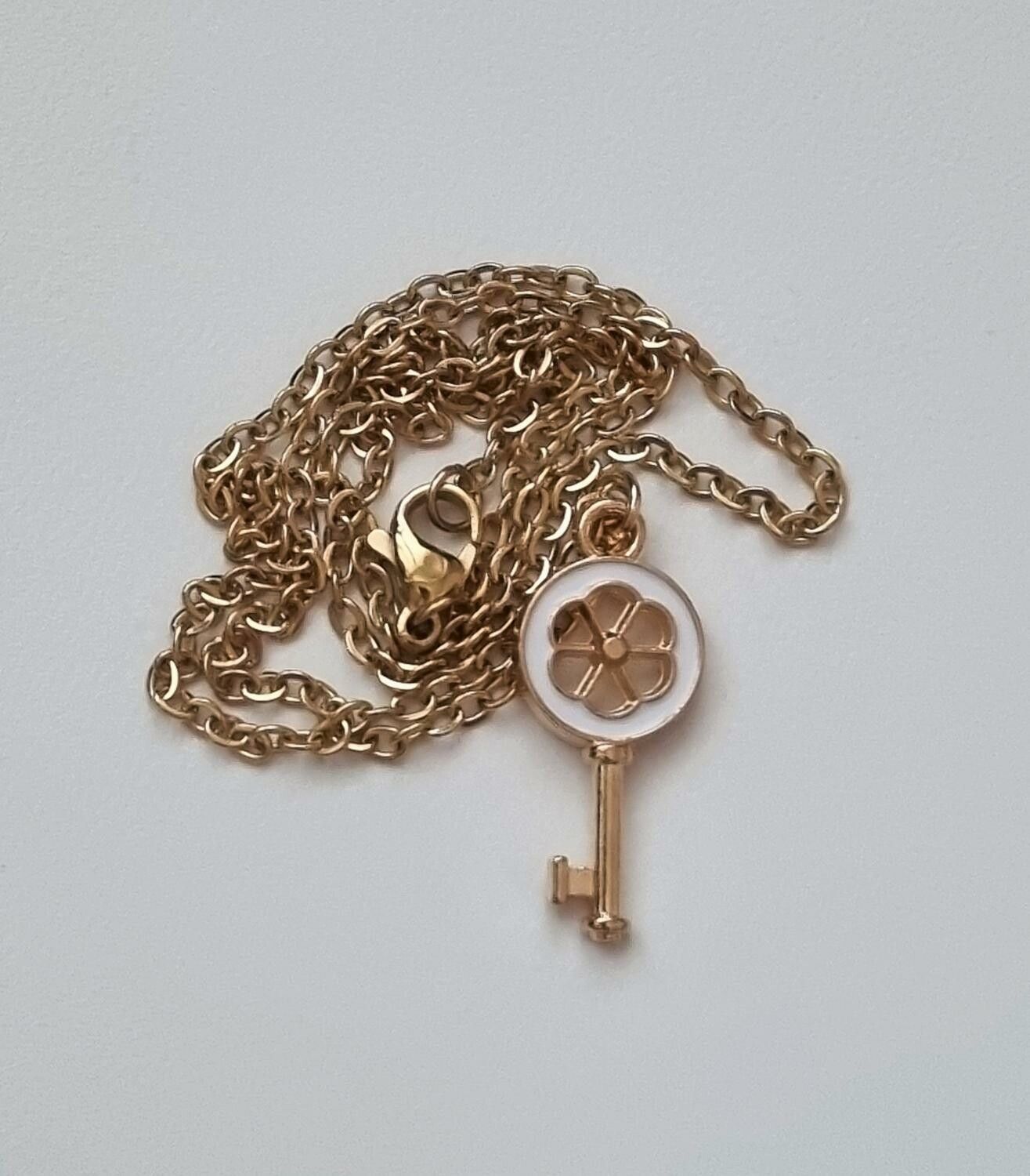 Guldfärgat halsband med en vit nyckel som berlock / charm