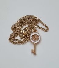 Guldfärgat halsband med en vit nyckel som berlock / charm