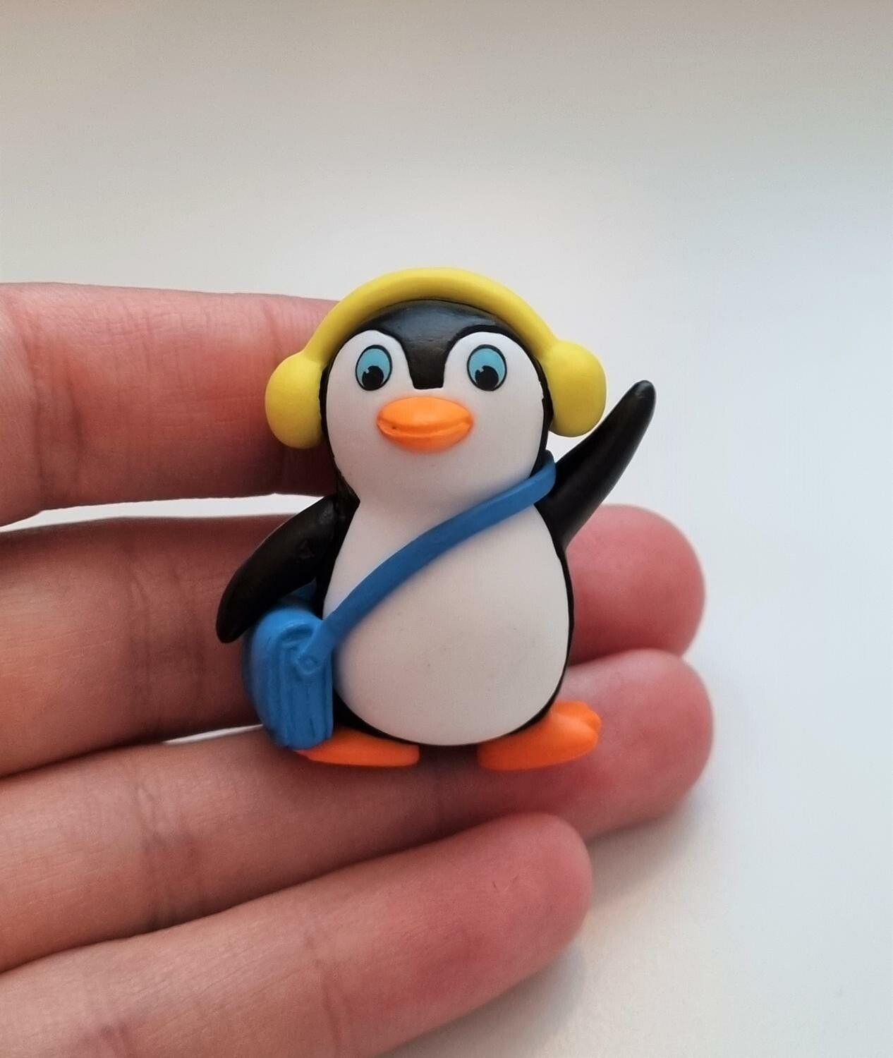 Pingvin med blå väska och gula öronvärmare. Miniatyr / figur för dekoration