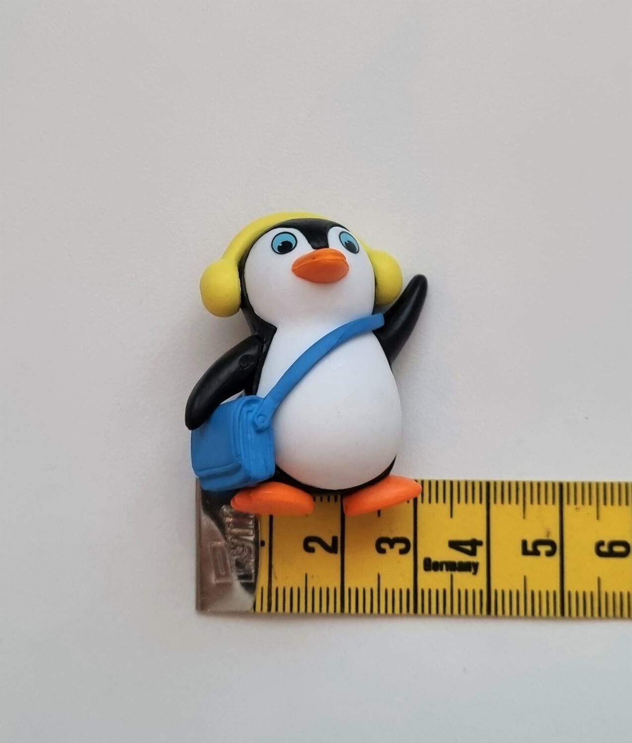 Pingvin med blå väska och gula öronvärmare. Miniatyr / figur för dekoration